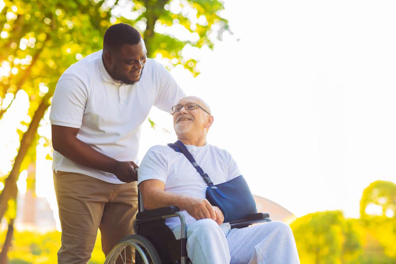Un assistant de vie dépendance se promenant avec un senior en fauteuil roulant 