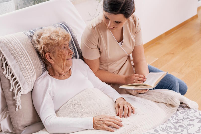 Une assistante de vie dépendance faisant la lecture à une personne âgée à son domicile