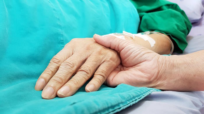 Personne tenant la main d'un senior alité et en fin de vie de la maladie de Parkinson