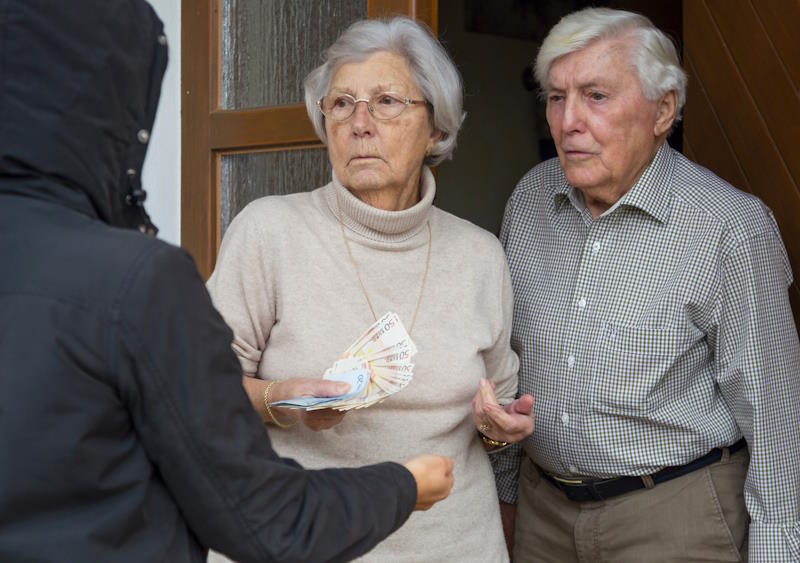 Couple âgé tenant des billets et les donnant à un escroc, victimes d'un abus de faiblesse