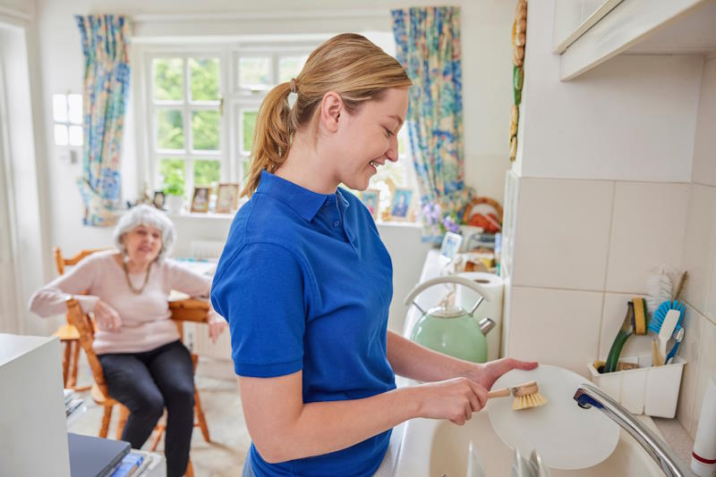 Aide à domicile faisant la vaisselle chez une dame âgée