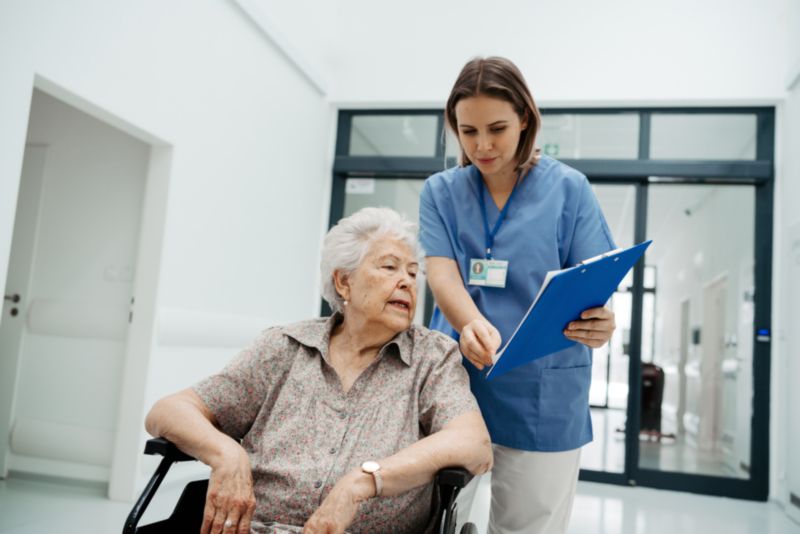 Personne âgée en fauteuil accompagnée d'une infirmière à sa sortie d'hôpital