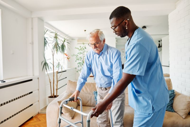 Senior avec un déambulateur aidé par un auxiliaire de vie à domicile