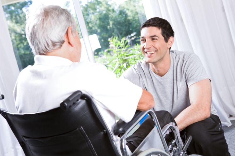 Senior en GIR 2 dans un fauteuil roulant pris en charge en EHPAD pr un soignant souriant